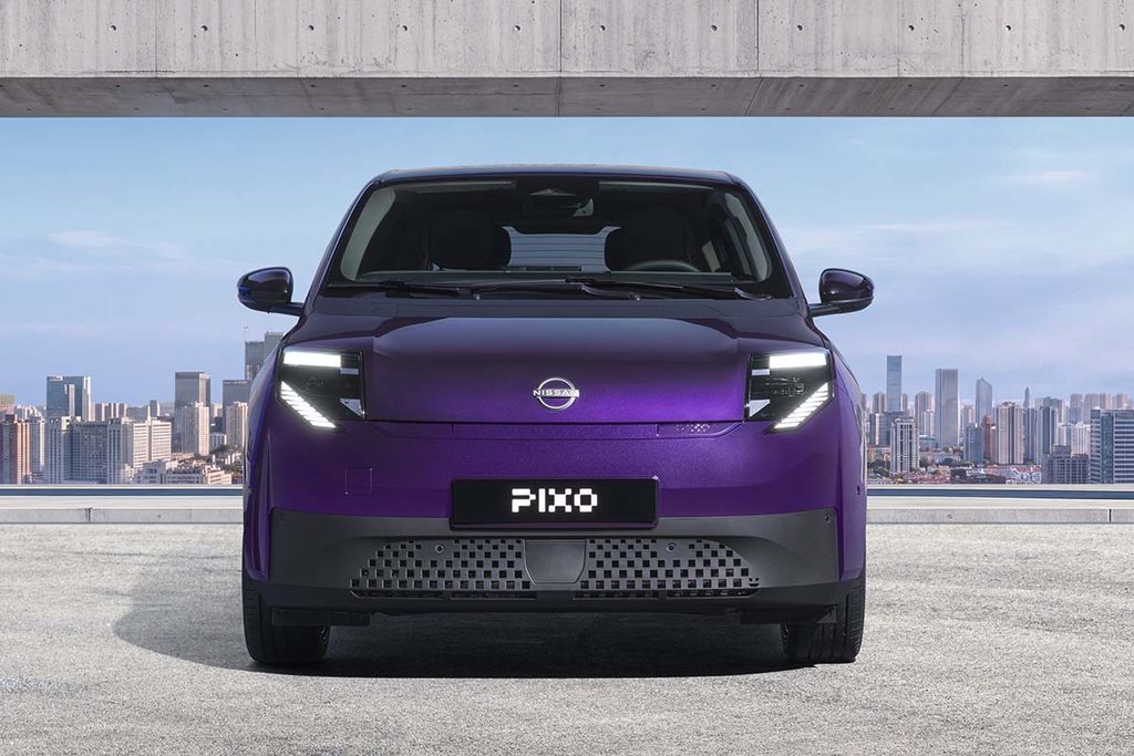 Photograph showcasing a purple Nissan Pixo concept car parked before a concrete architectural opening with a city skyline beyond. Front view highlights illuminated angular headlights, closed grille, PIXO plate, sleek compact design, and blue sky backdrop.